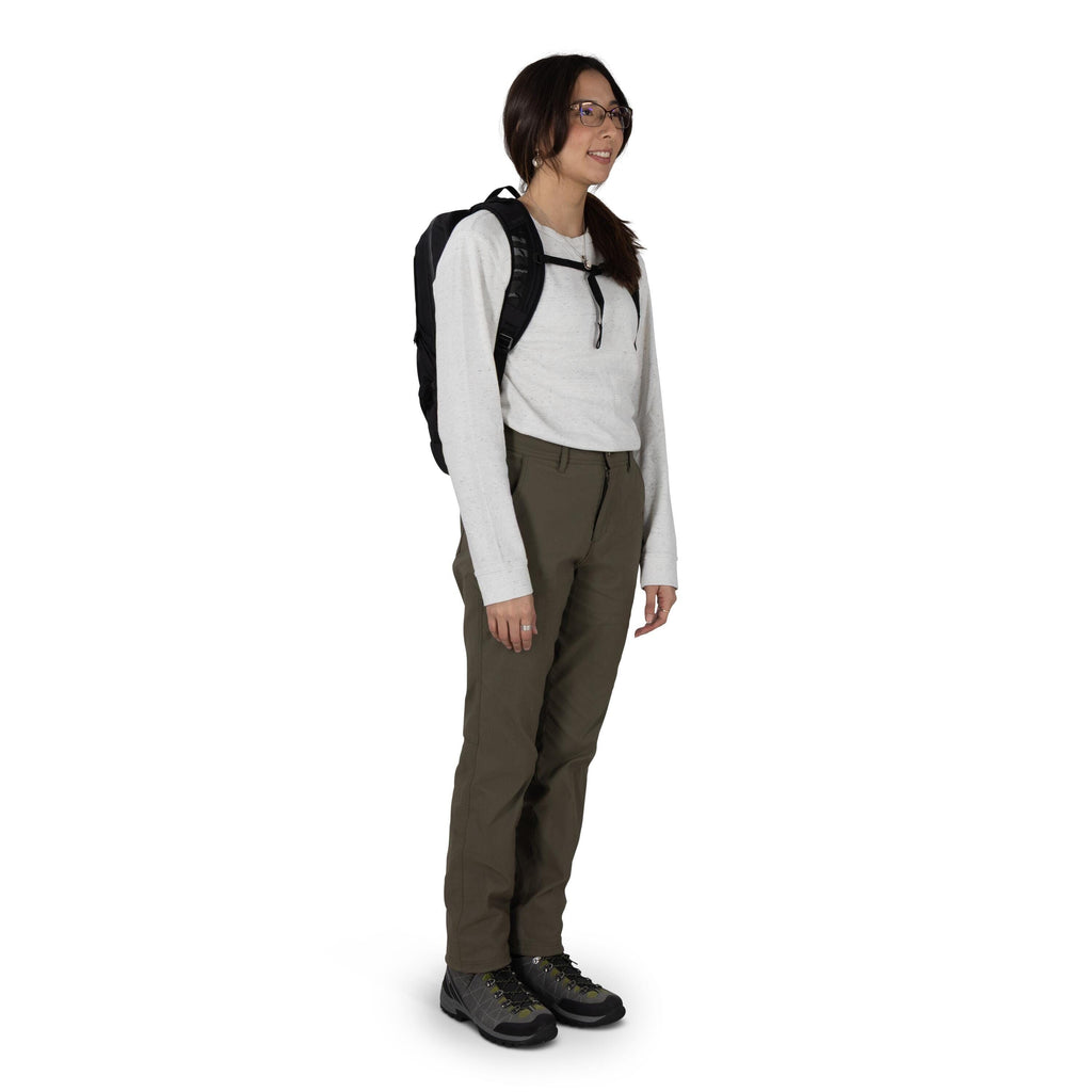 A person stands in a studio setting wearing outdoor clothing and a small black backpack. They have on a light gray long_sleeve shirt tucked into olive green hiking pants. The outfit is completed with gray hiking shoes featuring black toe caps and lime acc