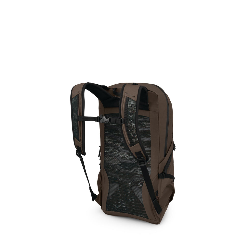 The image shows a brown backpack photographed from the back-right angle. It has padded shoulder straps with a chest buckle and a ventilated mesh back panel in a dark camo pattern. Side compression straps and a side zip pocket are visible, and the pack has