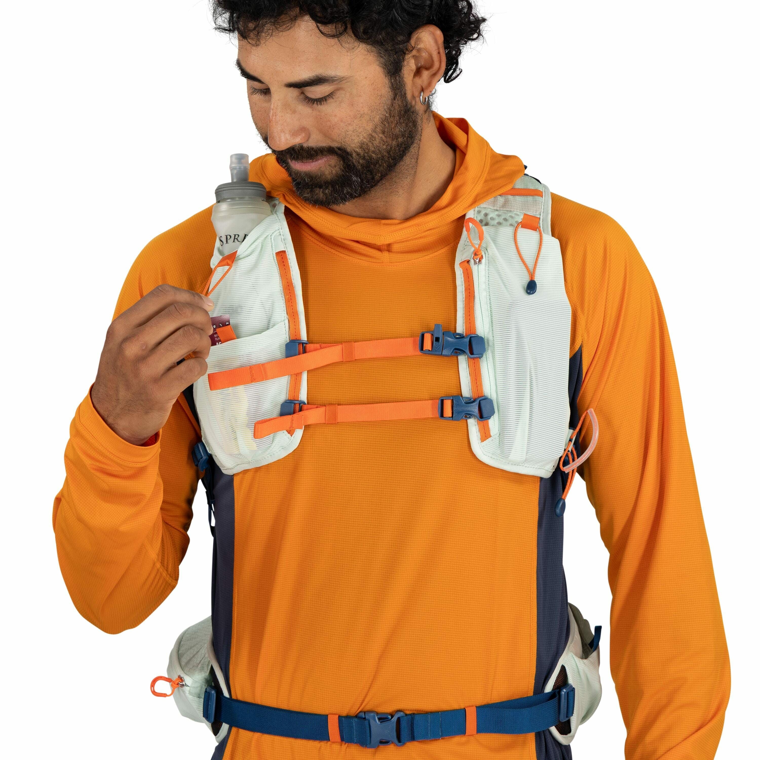The image shows a person wearing an orange long-sleeve athletic shirt and a multi-colored hydration vest, which is primarily light blue and orange with dark blue accents. The vest features several adjustable straps across the chest, secured with blue and