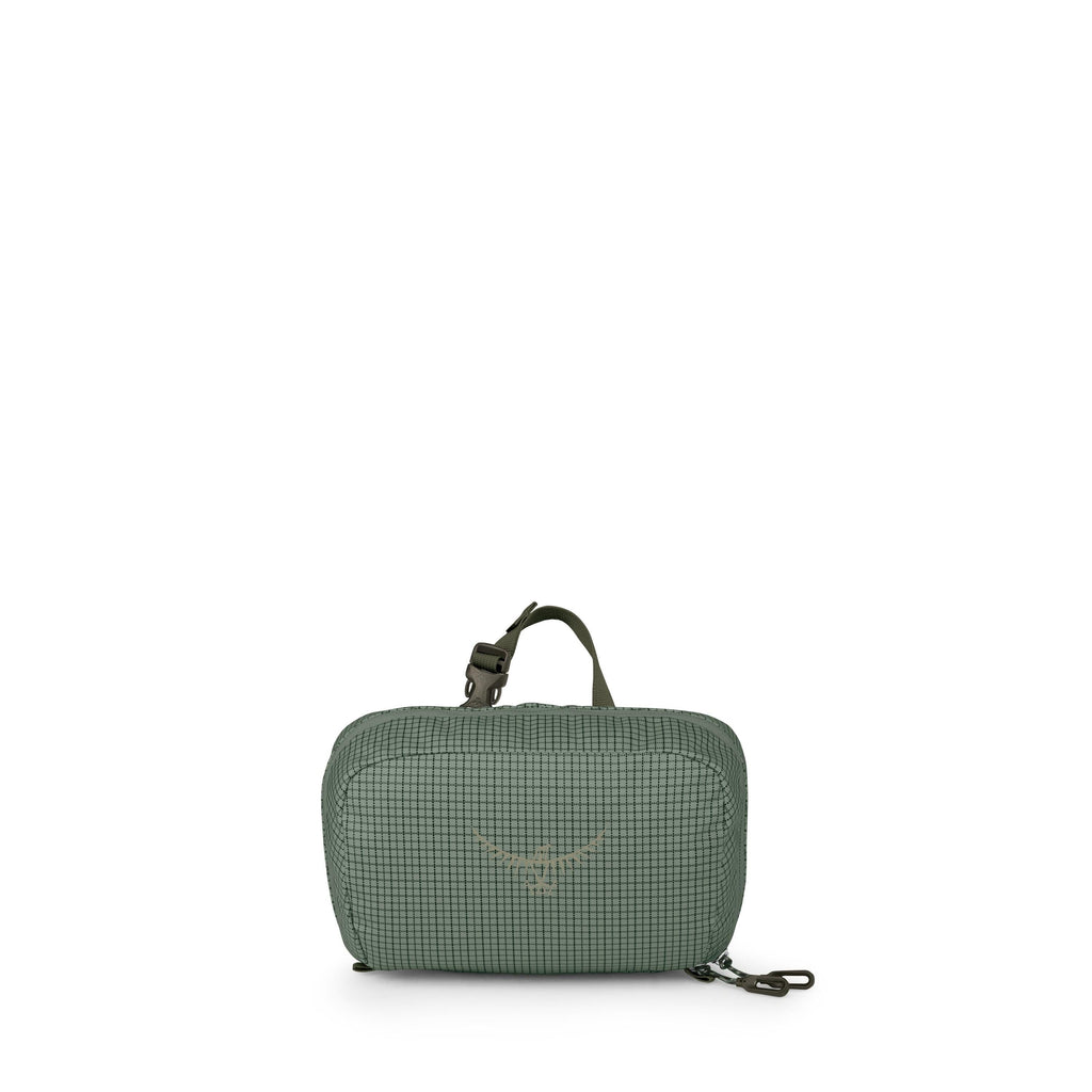 A small green zippered pouch sits centered against a white background. The fabric has a subtle checkered grid pattern and features a minimalist bird-like logo on the front. A short top handle and an adjustable strap clip with black hardware are visible on
