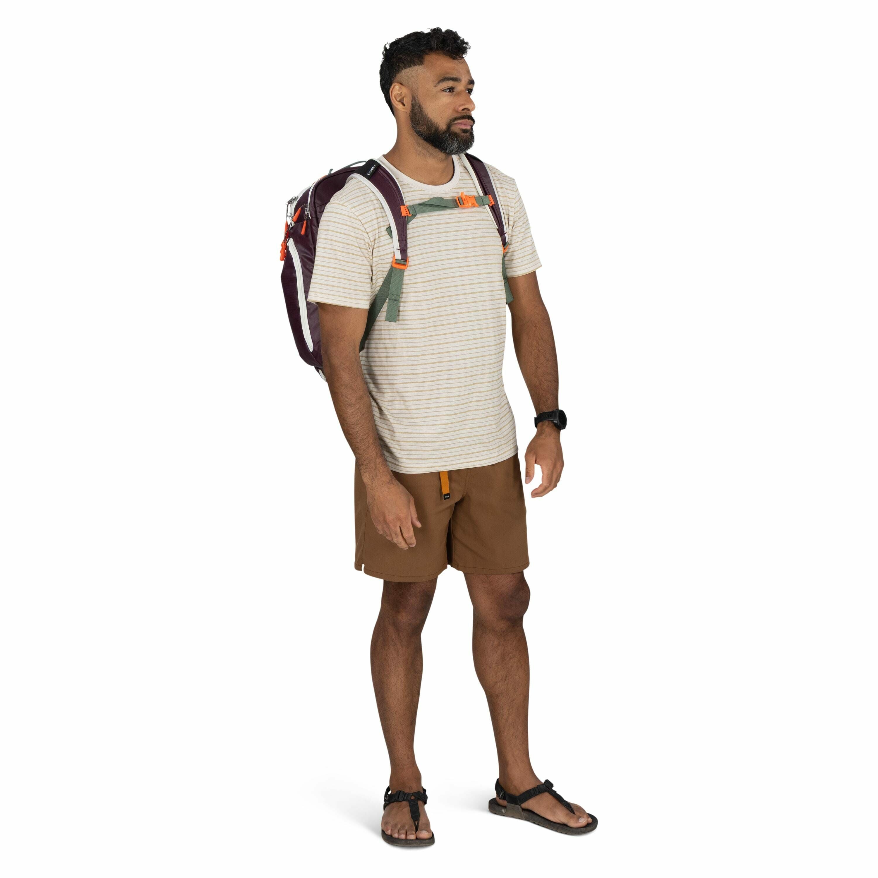 The image features a person standing against a plain white background, dressed in casual outdoor attire. The individual is wearing a light-colored, short-sleeved, striped t-shirt paired with brown shorts. They have on black sandals and a black watch on th