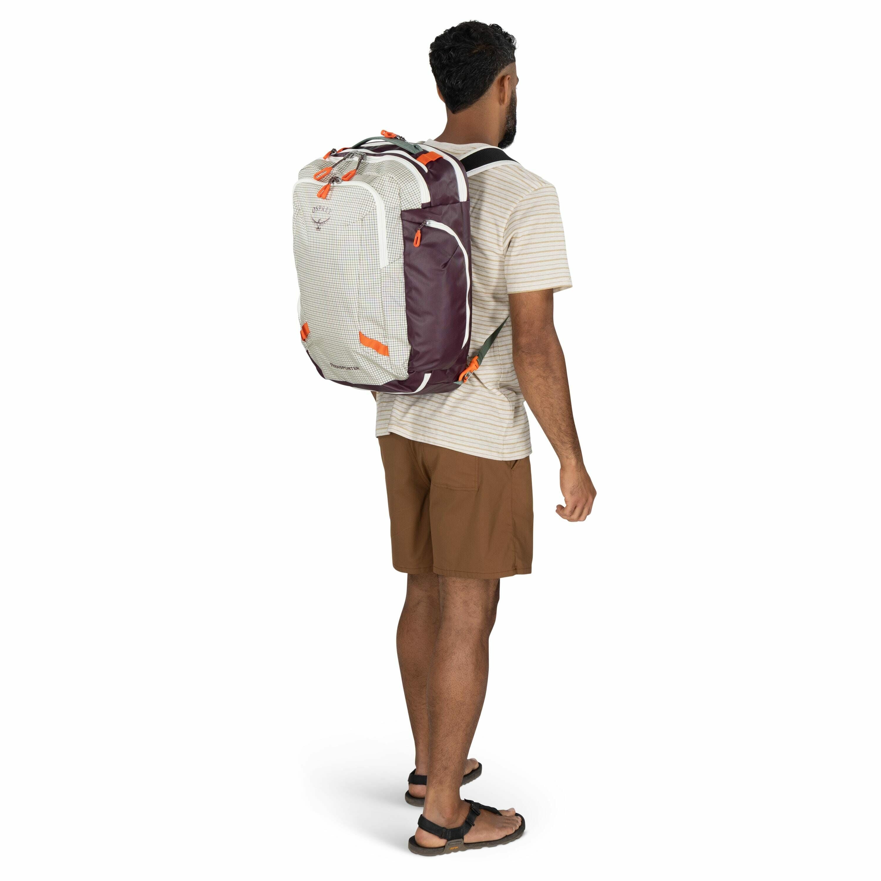 The image depicts a man from a rear three-quarter angle, wearing a casual outfit consisting of a light striped t-shirt, brown shorts, and sandals. He is carrying an Osprey backpack, which is predominantly white with maroon side panels and features orange