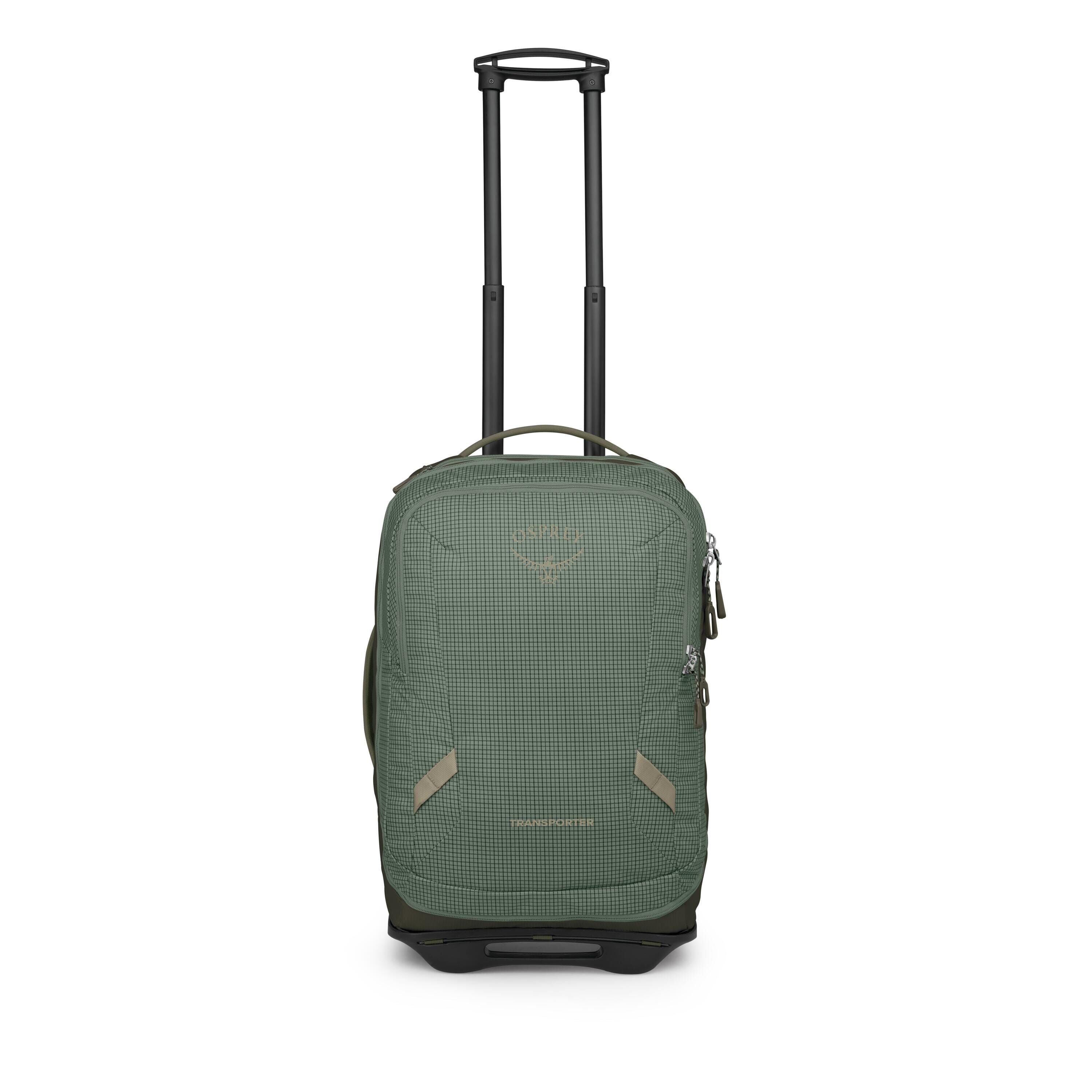 A compact green rolling suitcase is shown from the front with an extended black telescoping handle. The bag has a subtle grid pattern, two small diagonal lash points on the front, and multiple zippered compartments. Its base features a molded black frame