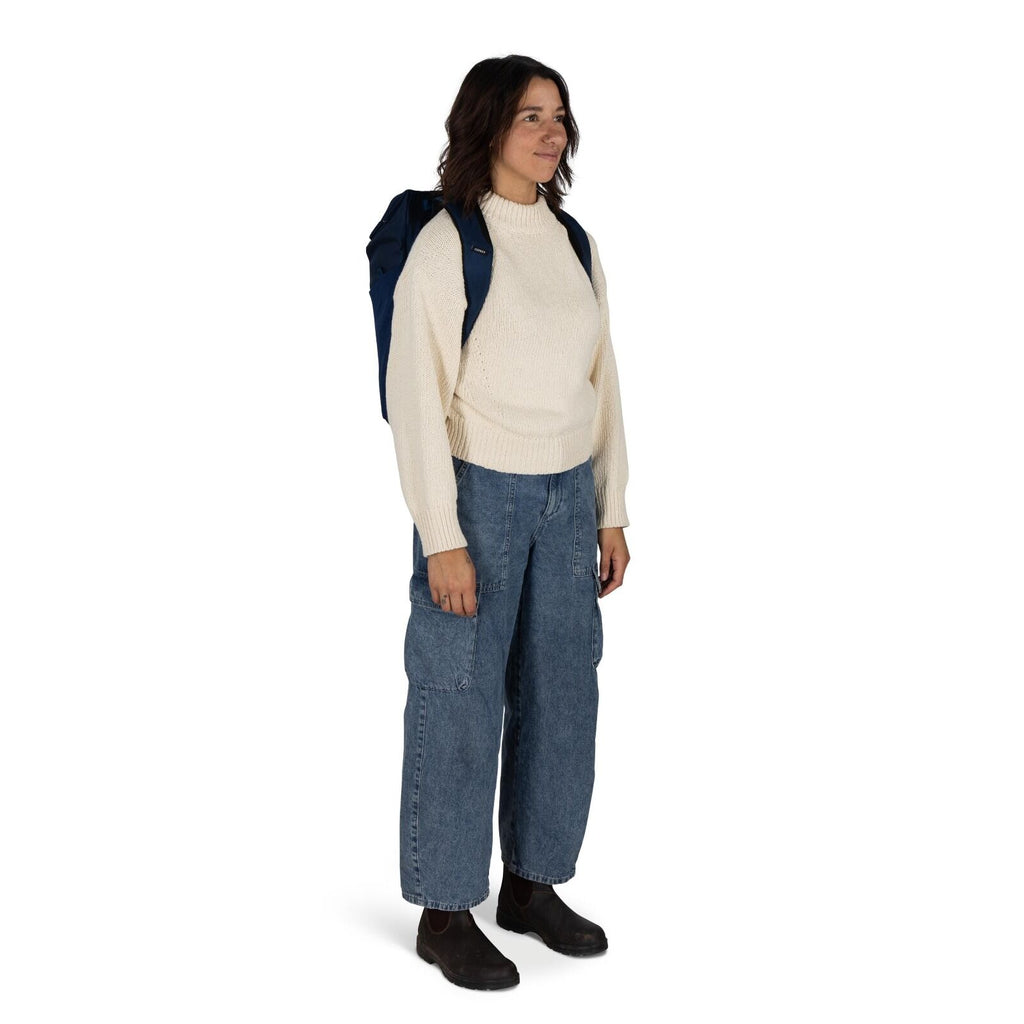 The image shows a person standing and facing slightly to the side. They are wearing a cozy, cream-colored knit sweater that appears warm and comfortable. The person is also wearing loose-fitting denim jeans with large pockets, giving a casual and relaxed