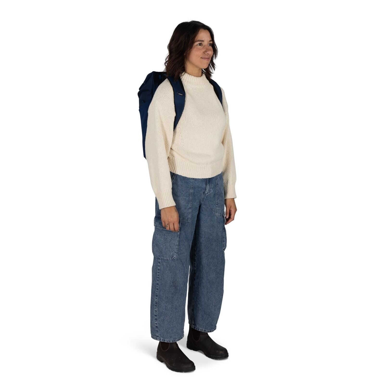 The image shows a person standing and facing slightly to the side. They are wearing a cozy, cream-colored knit sweater that appears warm and comfortable. The person is also wearing loose-fitting denim jeans with large pockets, giving a casual and relaxed