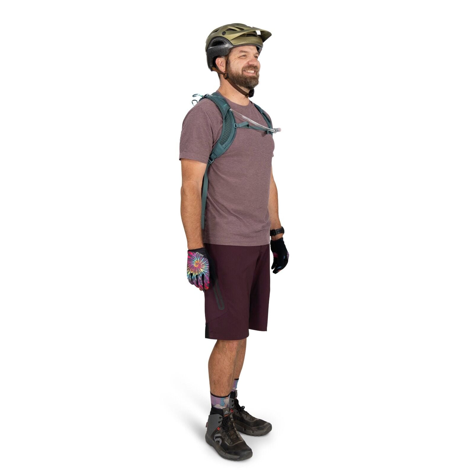 The image features a person dressed in biking attire, including a short-sleeve shirt and knee-length shorts in shades of purple. They are equipped with a green helmet for safety, and a backpack with a visible hydration tube, suggesting preparation for a l