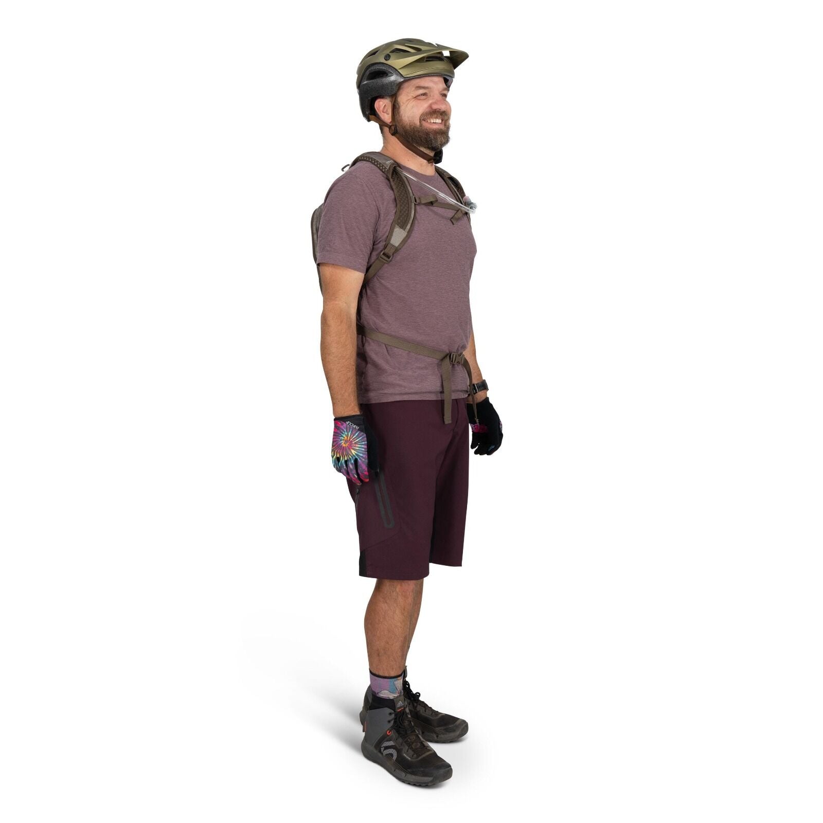 The image shows a man dressed in mountain biking gear, including a helmet and a hydration pack. He is wearing a purple T-shirt and burgundy shorts, and his hands are covered with colorful gloves featuring a tie-dye pattern. The man is also wearing hiking