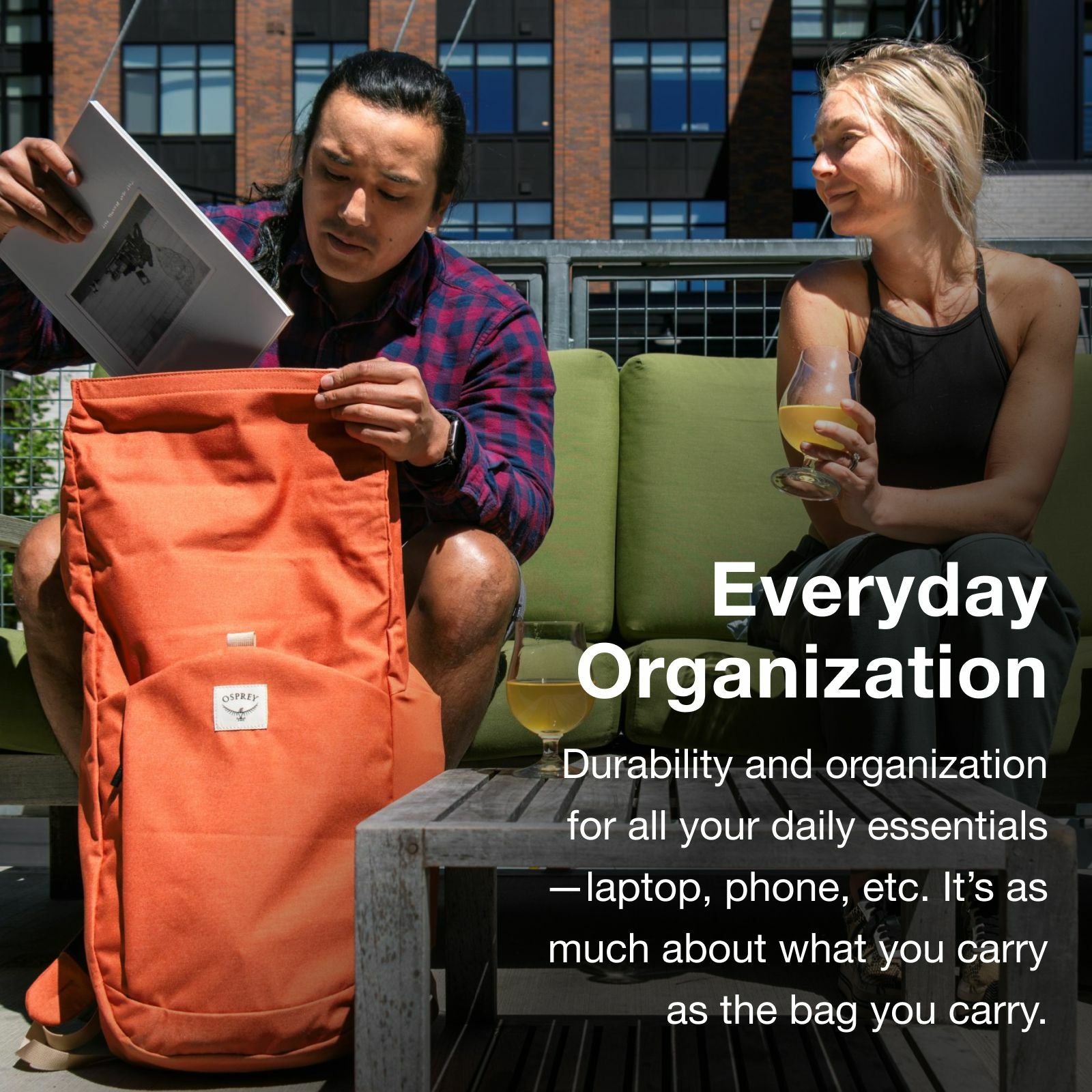 A person sits on a patio, opening an orange backpack while a woman enjoys a drink nearby, emphasizing everyday organization and durability.