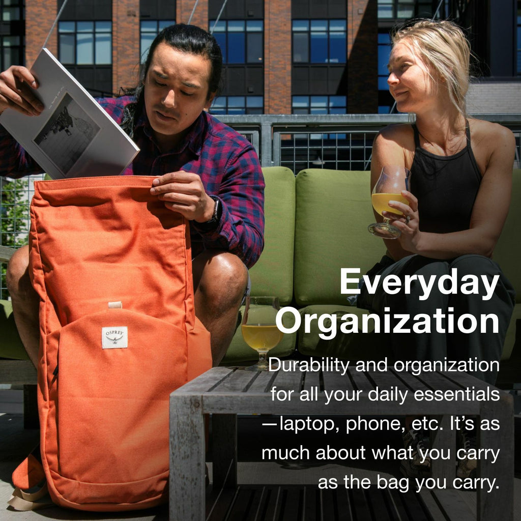 A person sits on a patio, opening an orange backpack while a woman enjoys a drink nearby, emphasizing everyday organization and durability.