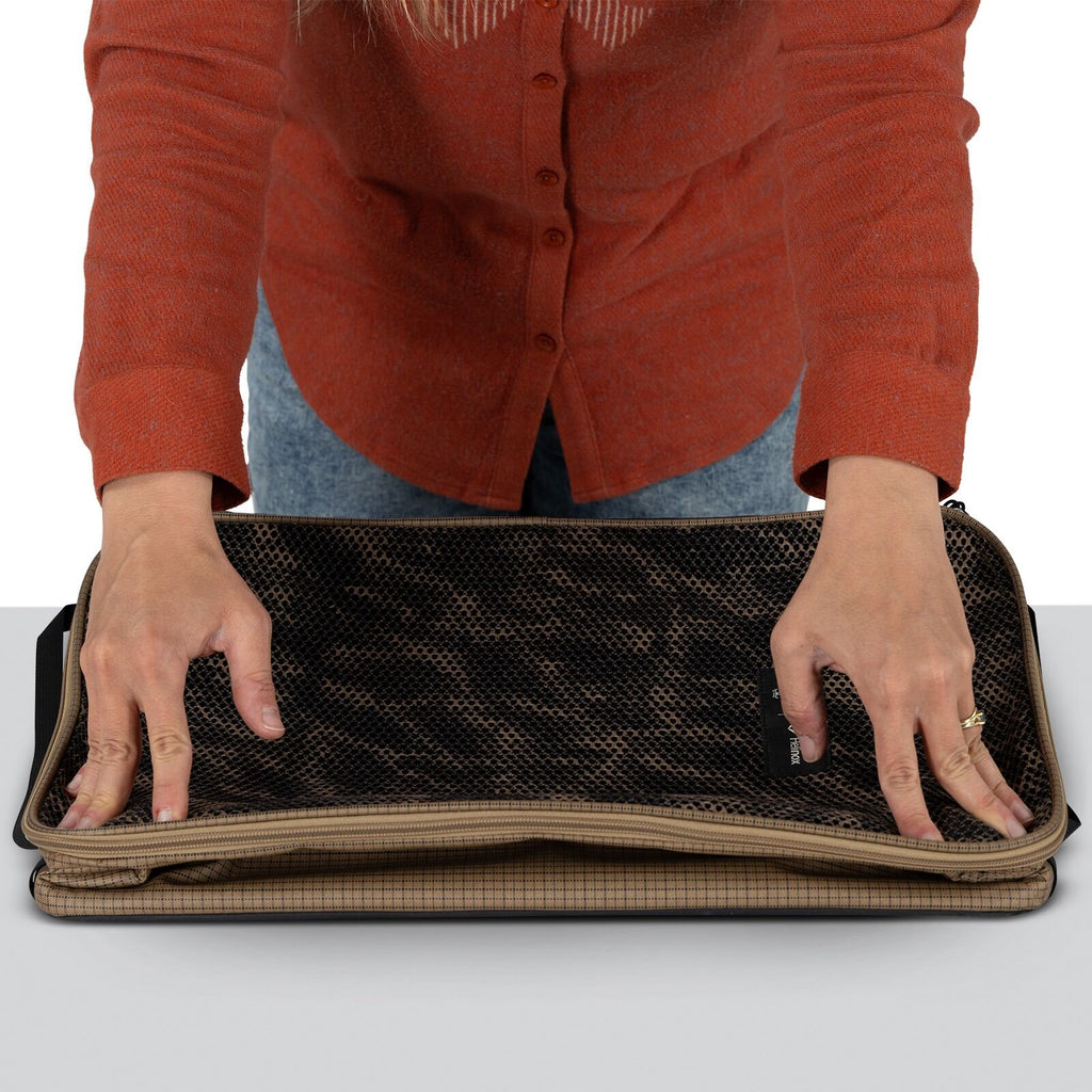 A person in a red shirt places a folded, checkered brown bag with a black mesh top on a gray surface, conveying an organized and focused action.