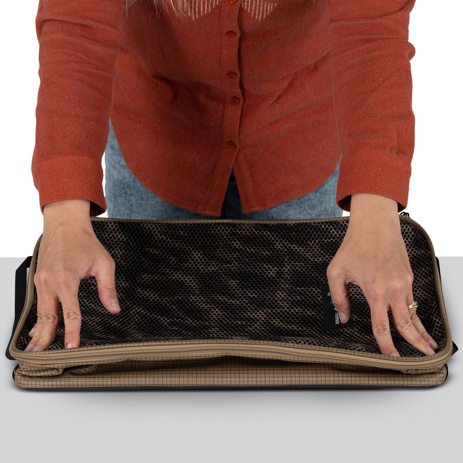 A person in a red shirt places a folded, checkered brown bag with a black mesh top on a gray surface, conveying an organized and focused action.