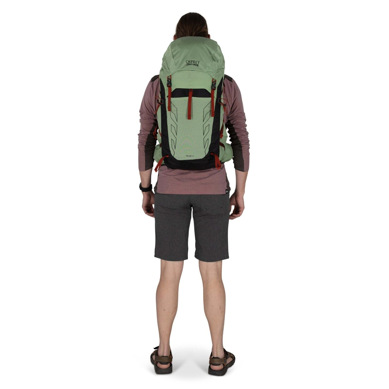 A person stands facing away, wearing a light green Osprey backpack and grey shorts, ready for an outdoor adventure.