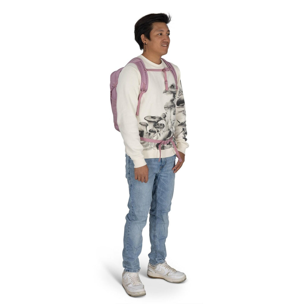 The image shows a person standing in a casual pose. They are wearing a cream-colored sweatshirt with a mushroom design printed on it, paired with light blue jeans. They are also carrying a dusty pink backpack, which adds a pop of color to their outfit. On