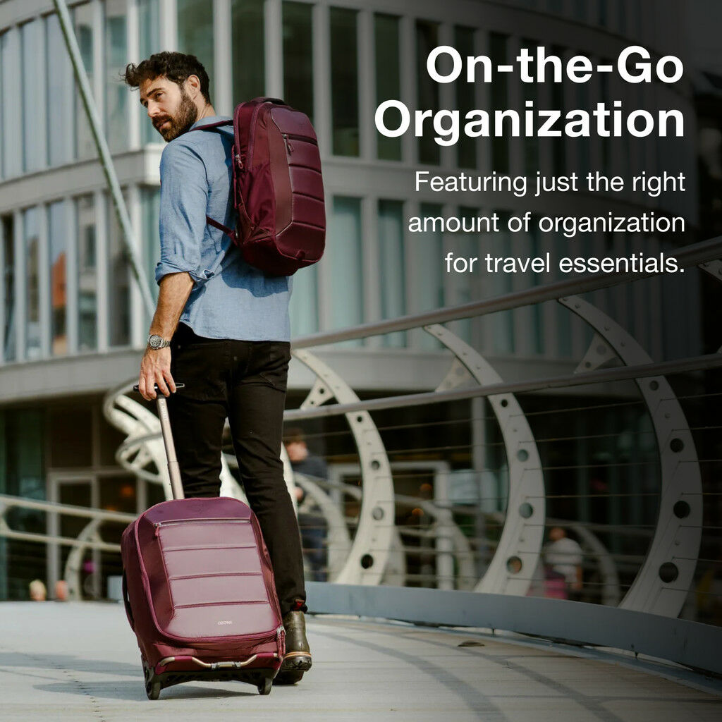 Man with burgundy luggage on a city bridge with modern architecture in the background.