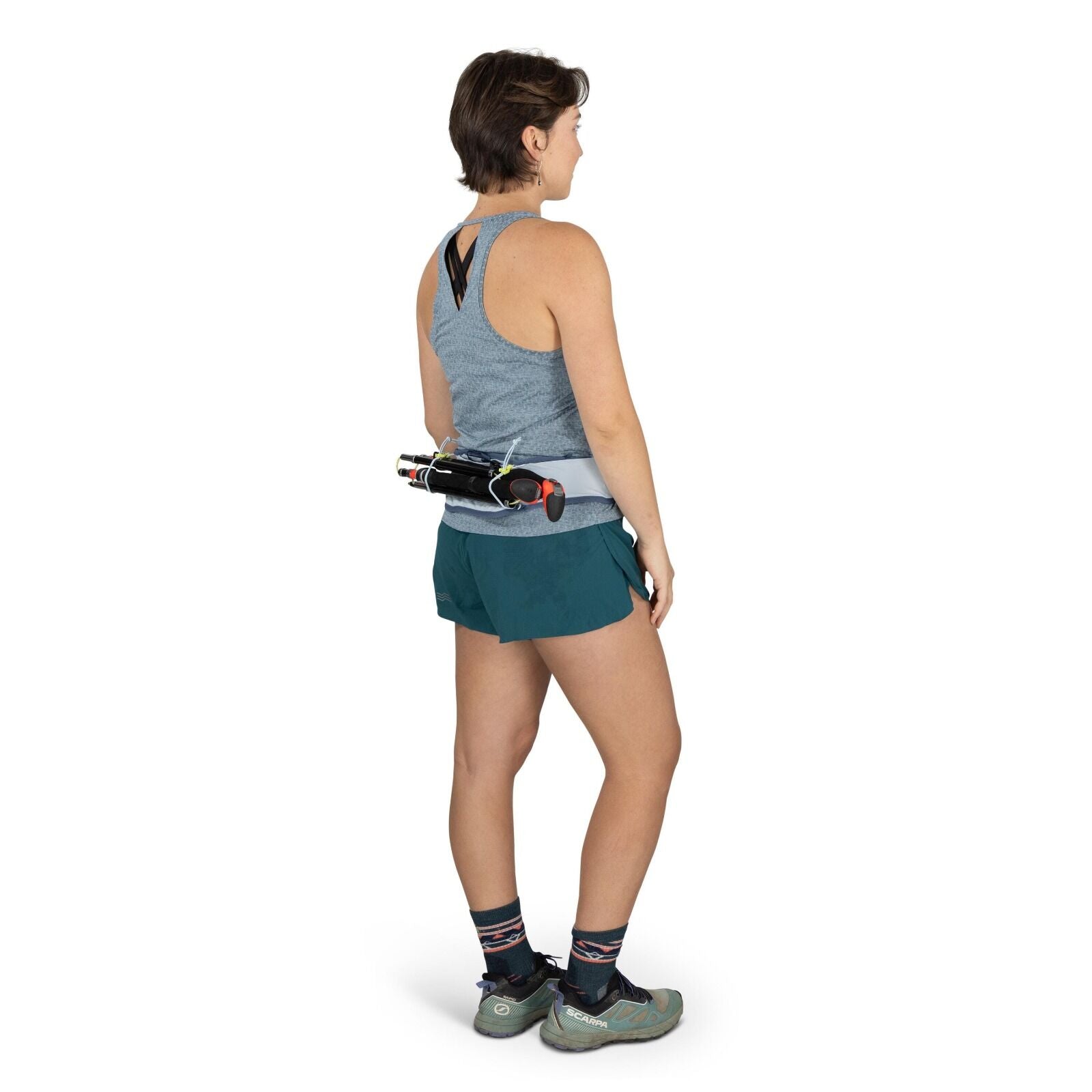 The image features a person standing in a side pose, wearing athletic attire suitable for running or hiking. The person is dressed in a gray sleeveless top with a cutout detail at the back, paired with teal shorts. On their feet are a pair of light green