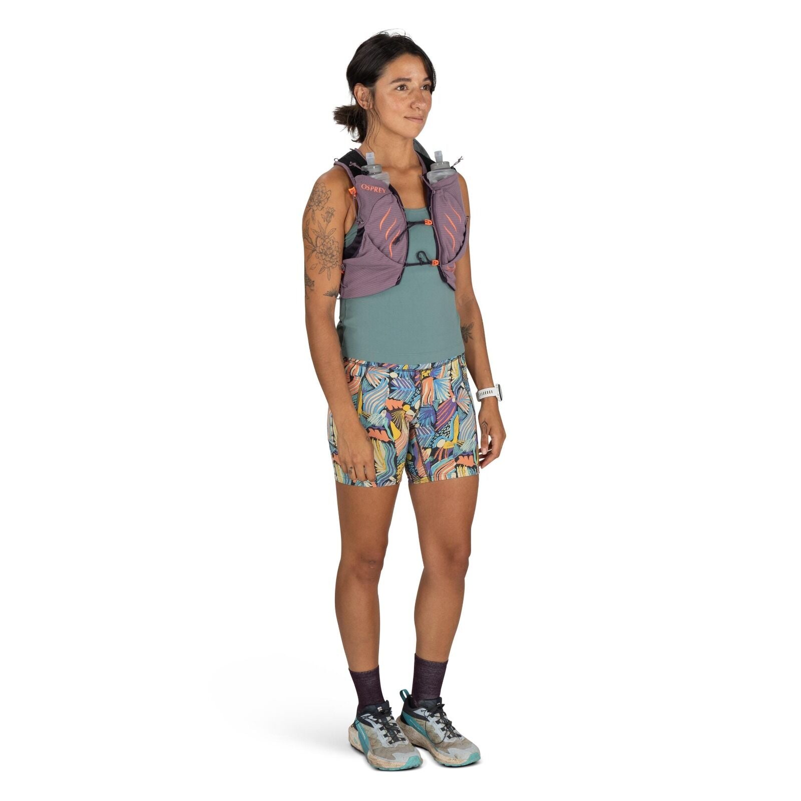 The image features a person standing in a neutral pose, dressed in athletic gear suitable for running or hiking. They are wearing a sleeveless teal top and colorful shorts with a lively, abstract pattern that combines various shades of blue, yellow, pink,