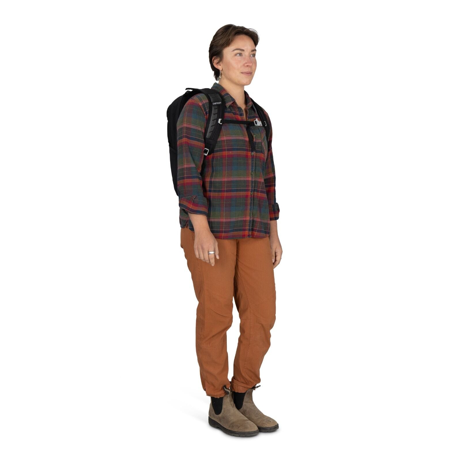 Person wearing a plaid shirt, brown pants, and a black backpack stands confidently, gazing forward. The tone is outdoorsy and casual.
