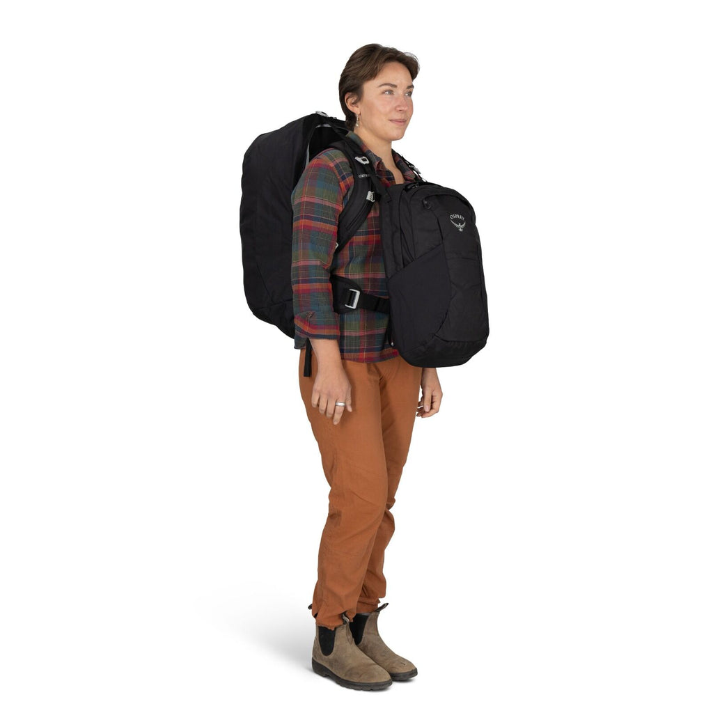 A person wearing a plaid shirt and brown pants carries a large black backpack and a smaller front pack. The tone is practical and adventurous.
