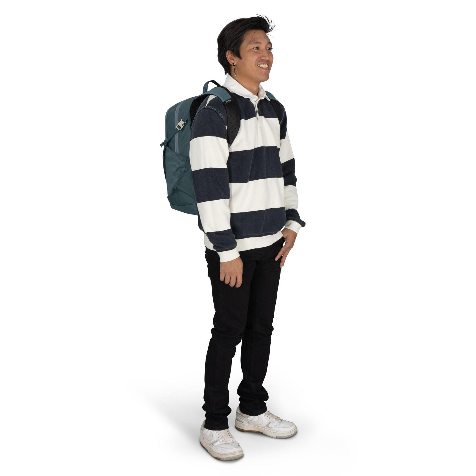 The image shows a person standing in a side profile pose wearing a casual outfit. They are dressed in a long-sleeve rugby-style shirt with broad horizontal navy blue and white stripes. The individual is also wearing slim-fit black pants and white sneakers