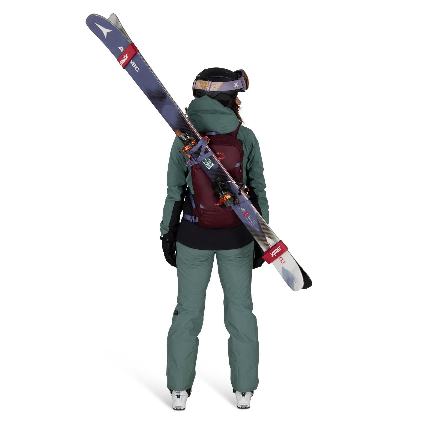 The image shows a person dressed in ski gear, viewed from the back. They are wearing a teal-colored ski jacket and pants, with a maroon backpack that securely holds a pair of skis diagonally across their back. The individual is also wearing black gloves a