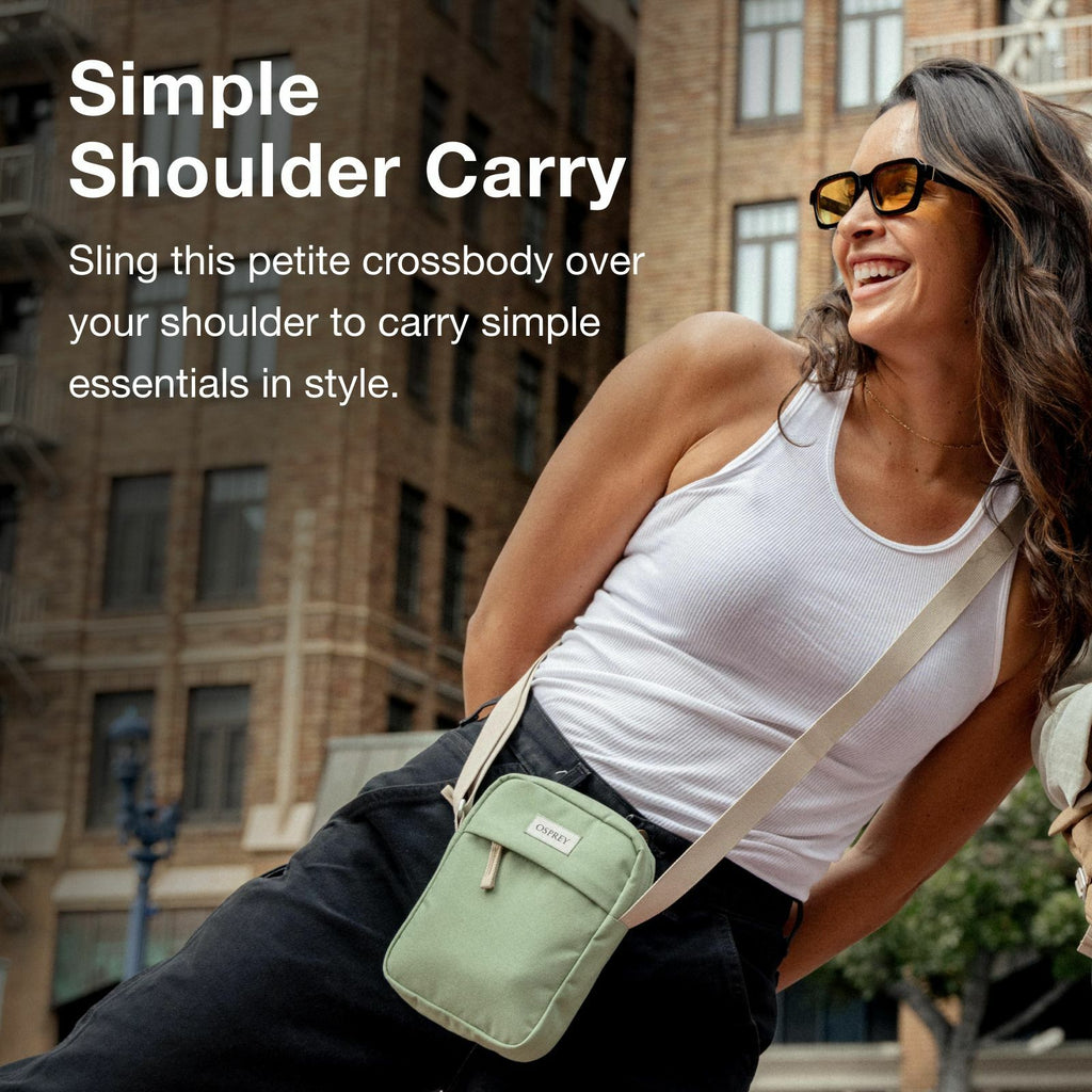A person models a stylish mint green crossbody bag, showcasing a trendy outfit against an urban backdrop with tall buildings.