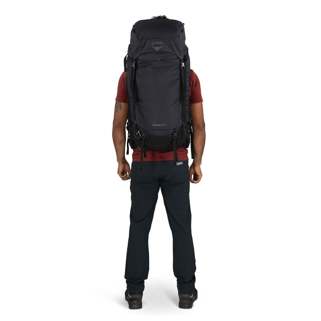 The image features a person standing with their back facing the camera, wearing a large backpack designed for hiking or outdoor adventures. The backpack is black and prominently displays the Osprey logo near the top, with "Kestrel 70" written below it, in