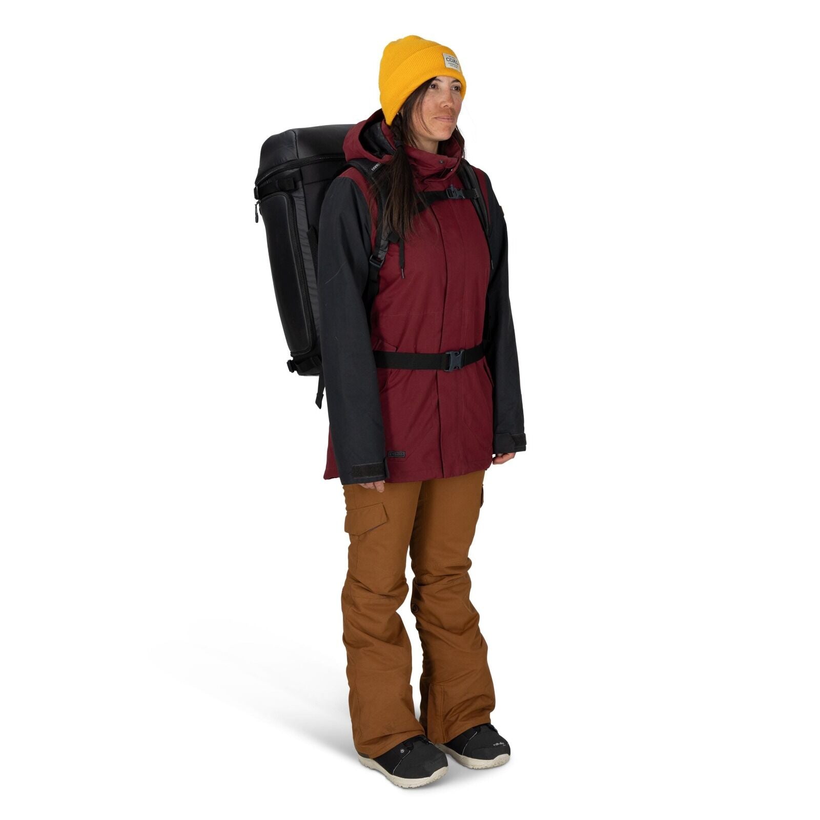 The image depicts a person dressed in outdoor winter clothing, suitable for a hiking or camping expedition. They are wearing a red jacket with black sleeves, brown pants, and black shoes, accompanied by a large black backpack. A bright yellow beanie adorn