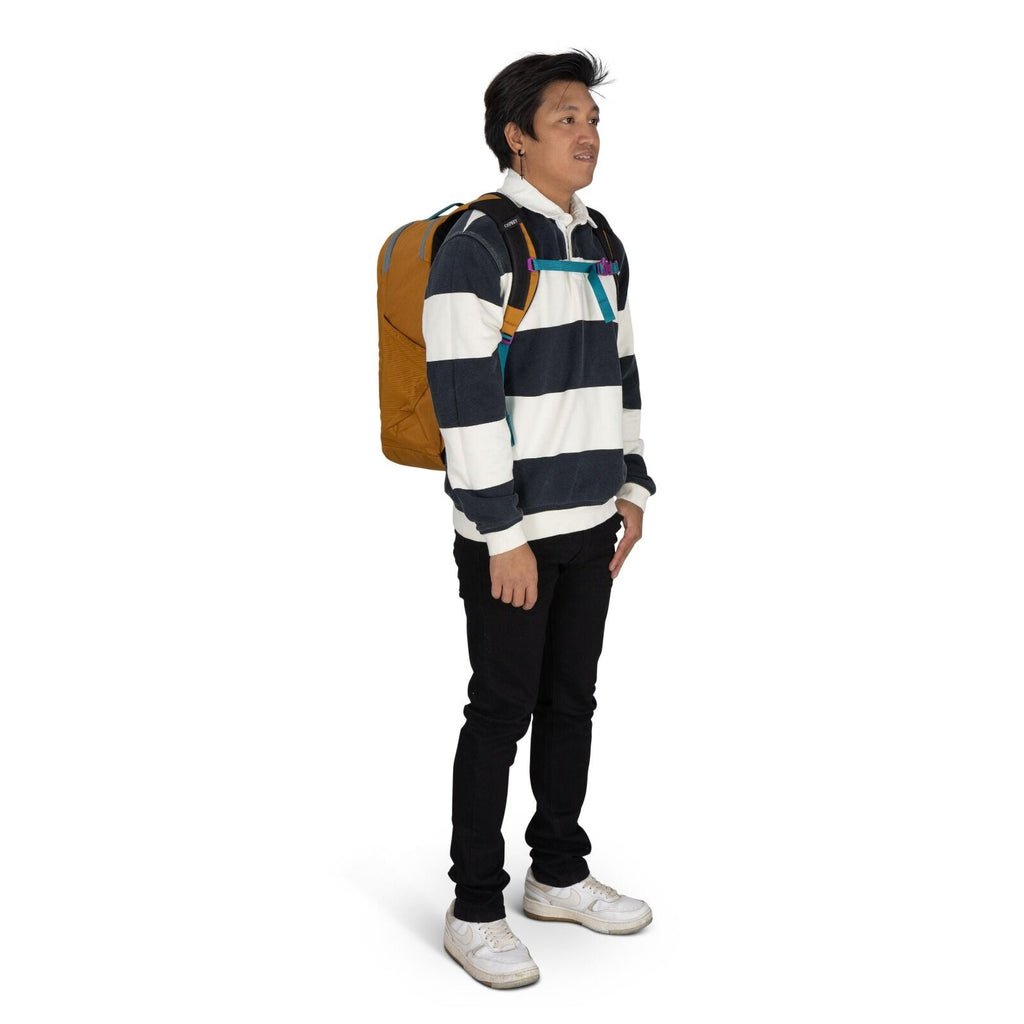 The image shows a person standing and facing slightly to the side, dressed in a casual outfit suitable for everyday wear. They are wearing a long-sleeve, white and dark blue striped rugby-style pullover, paired with black pants. On their feet are white sn