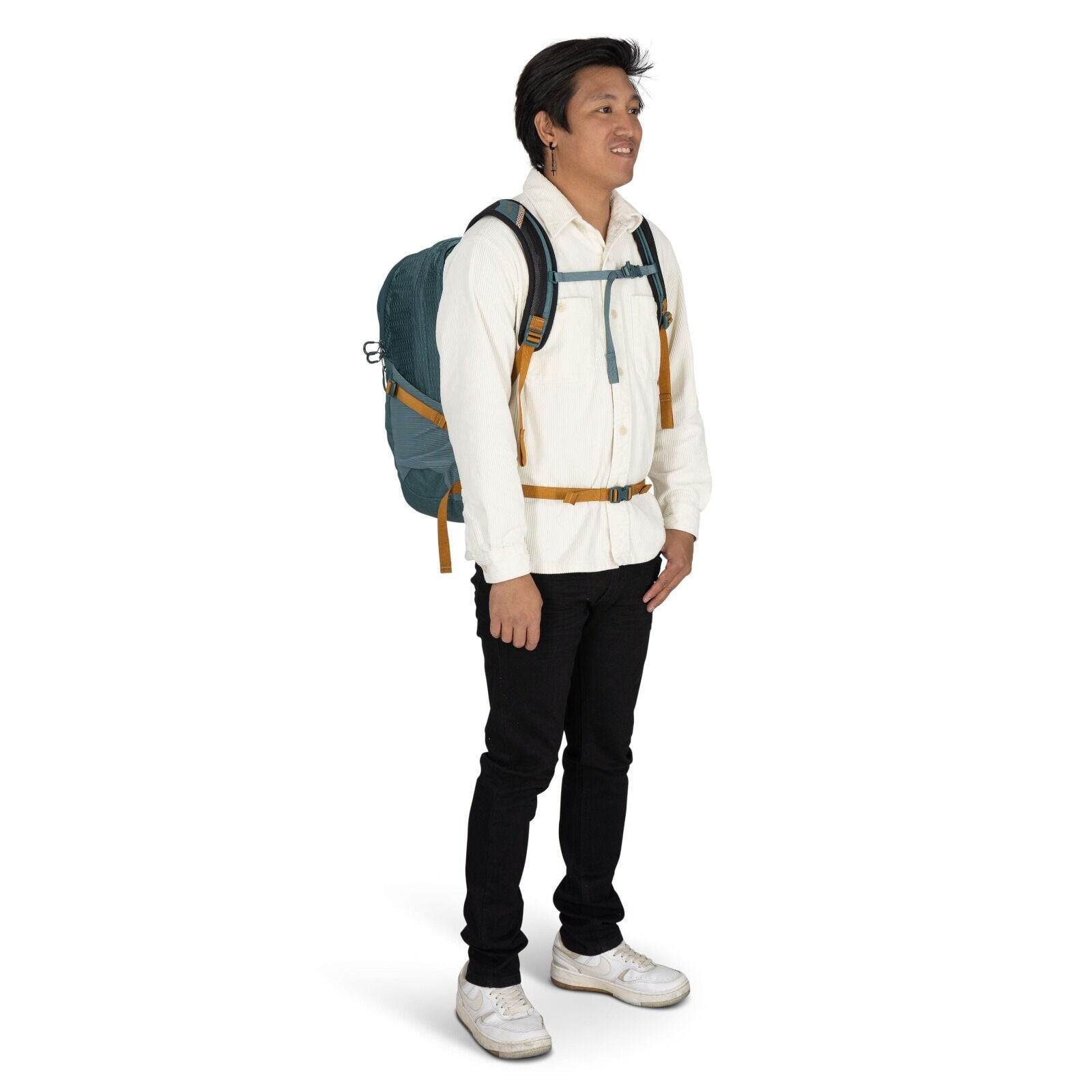 The image depicts a man standing wearing casual attire suitable for an outdoor or travel setting. He is wearing a white shirt with buttoned pockets and black pants, paired with white sneakers that have slight wear marks, suggesting frequent use. He is car