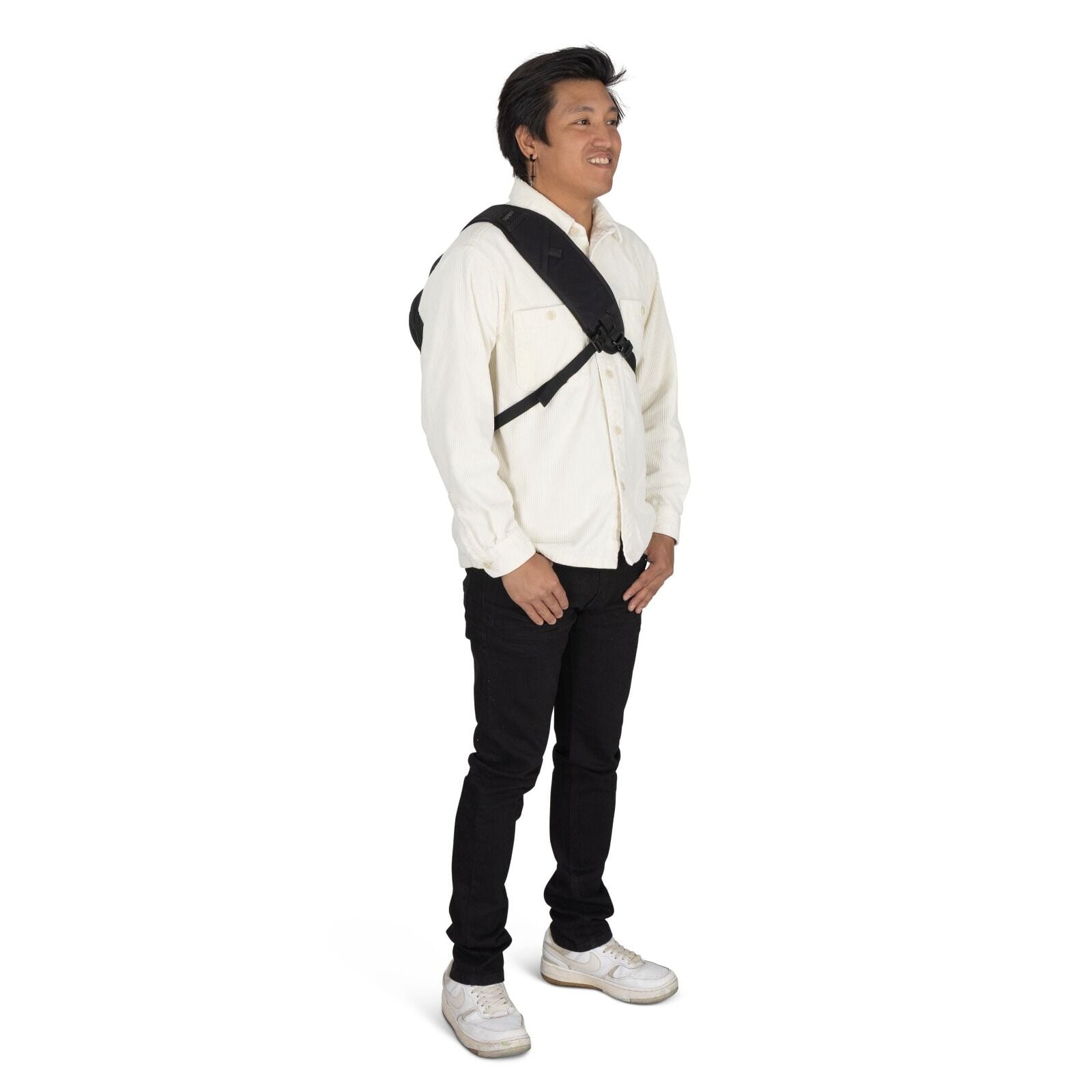 The image features a person standing with a relaxed posture. They are dressed in a light beige button-up shirt paired with black jeans and white sneakers, giving off a casual yet put-together look. The individual is carrying a black backpack with a single