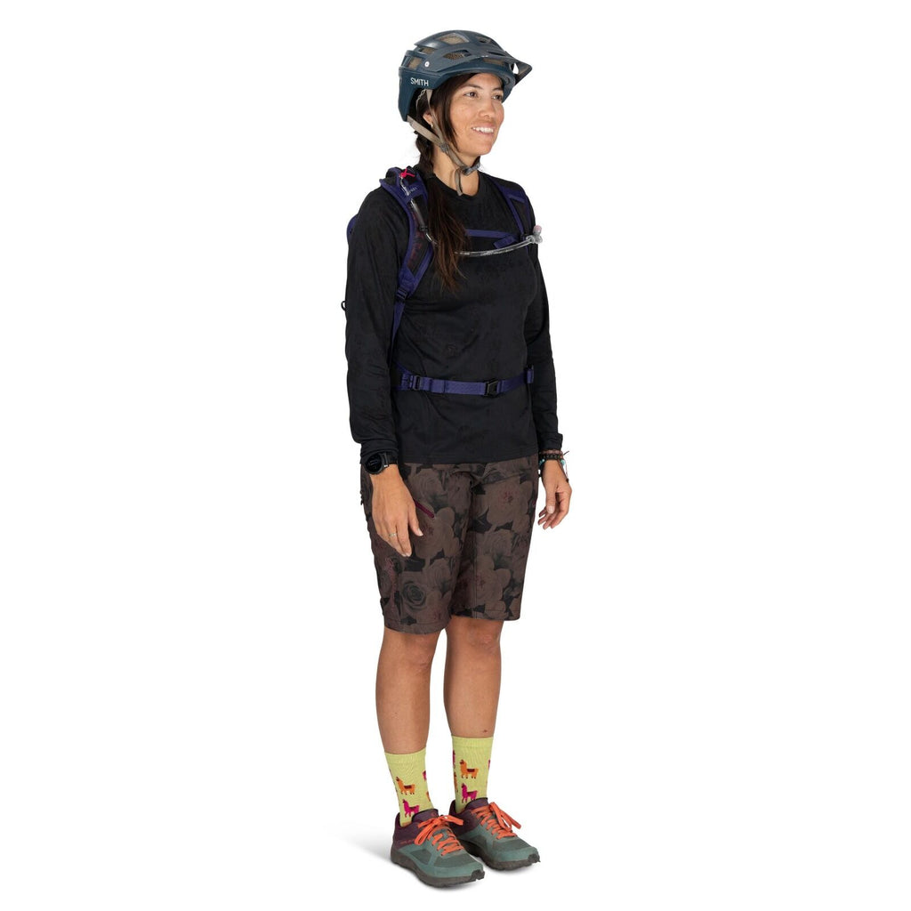 The image depicts a person dressed in outdoor sports attire, suitable for mountain biking or a similar activity. They are wearing a black long-sleeved shirt, camouflage-patterned shorts, and neon yellow socks adorned with red and purple llama patterns. Th