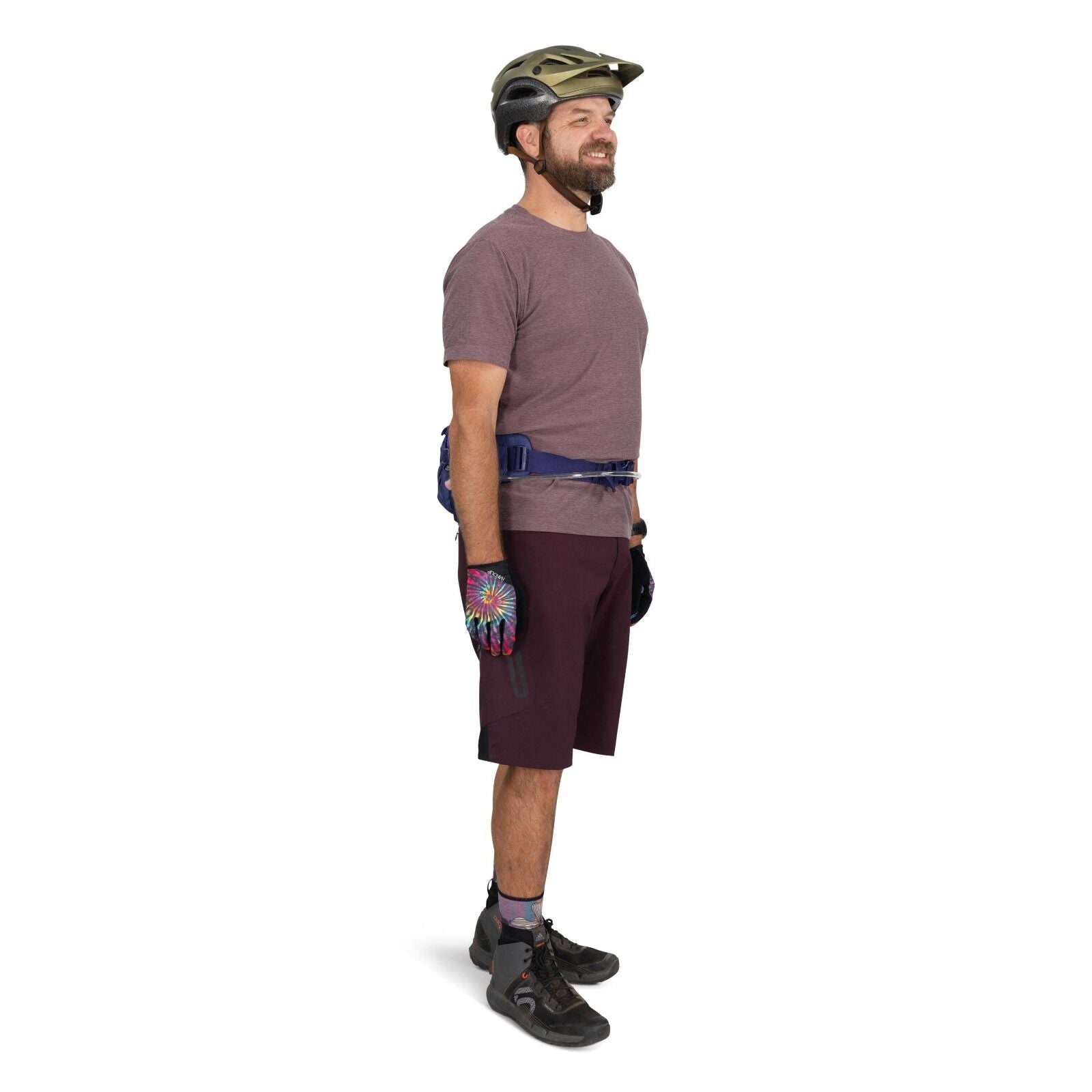 The image depicts a person standing in a side profile view. They are wearing a gray helmet and a plain purple t-shirt along with dark purple knee-length shorts. The individual is equipped with colorful gloves featuring a multicolored, tie-dye pattern and