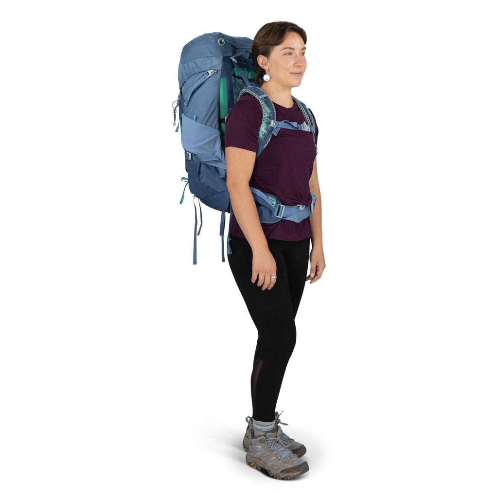 The image shows a person dressed in outdoor apparel, ready for a hiking adventure. They are wearing a purple short-sleeved shirt and black leggings, paired with sturdy gray hiking boots that offer support and traction for rugged terrains. On their back is