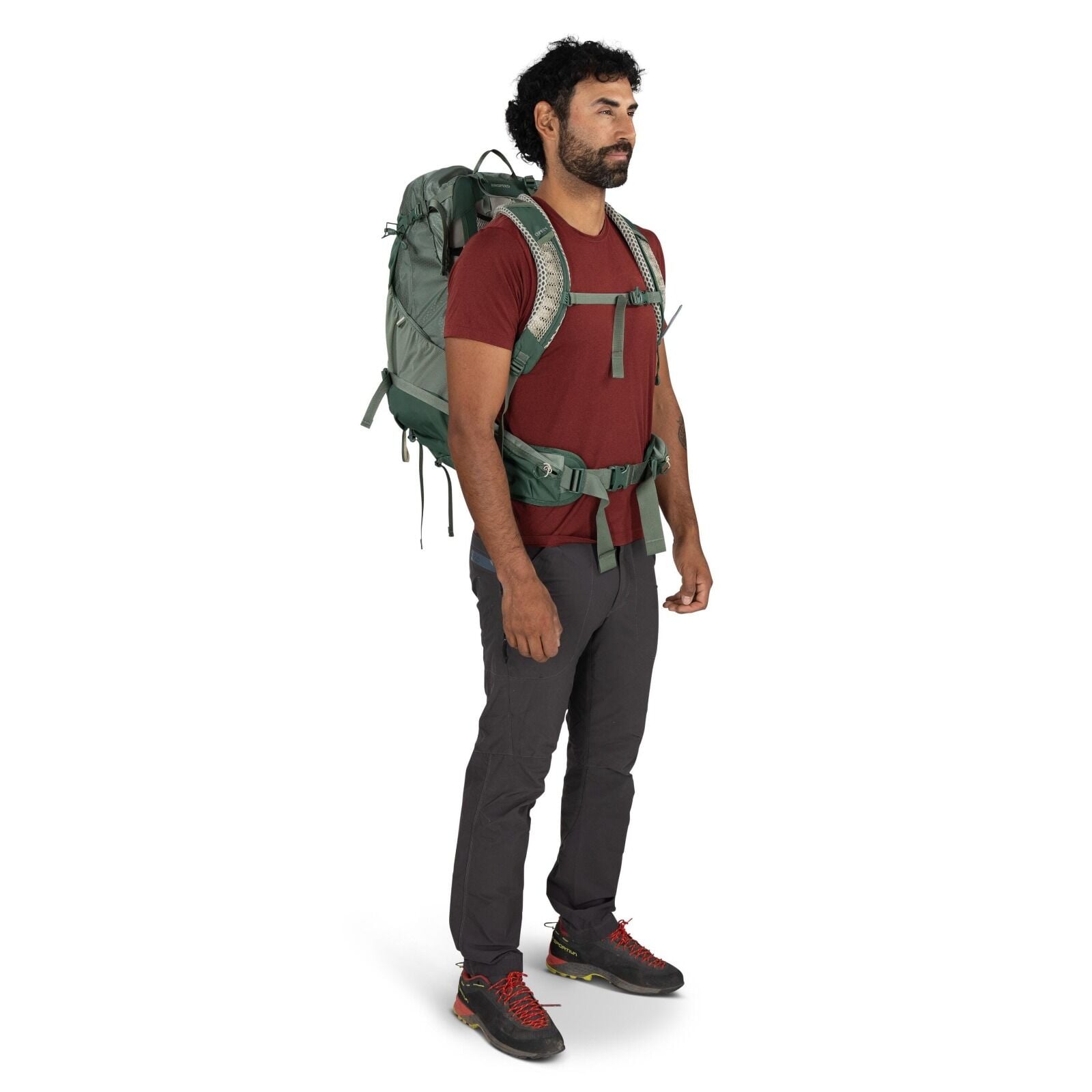 The image features a person dressed in outdoor attire, likely prepared for hiking or trekking. They are wearing a red short-sleeve t-shirt and dark gray hiking pants. On their feet are black shoes with red laces and subtle green accents, suggesting they a
