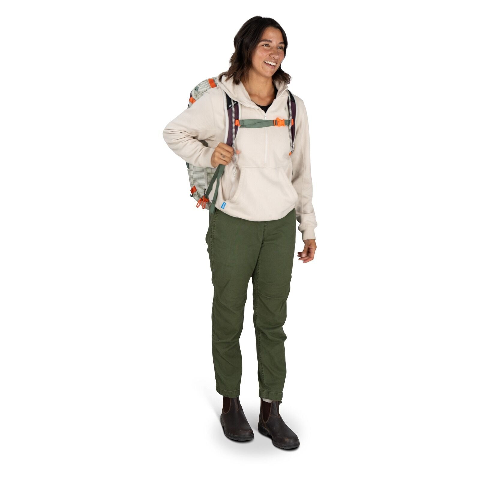 The image features a person standing and holding a duffel bag in one hand. The individual is dressed in a light-colored hooded sweatshirt, olive green pants, and brown boots. The duffel bag is predominantly light-colored with purple ends and features oran