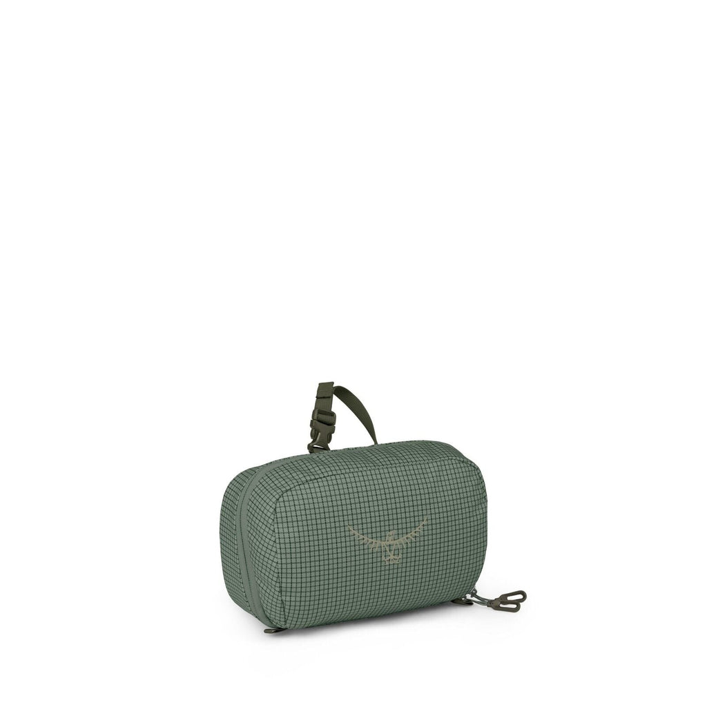 A small green travel pouch is shown from multiple angles against a white background. The bag has a subtle grid pattern, rounded edges, and a compact rectangular shape. It features dual zippers, a small top strap with a buckle, and a detachable clip seen s