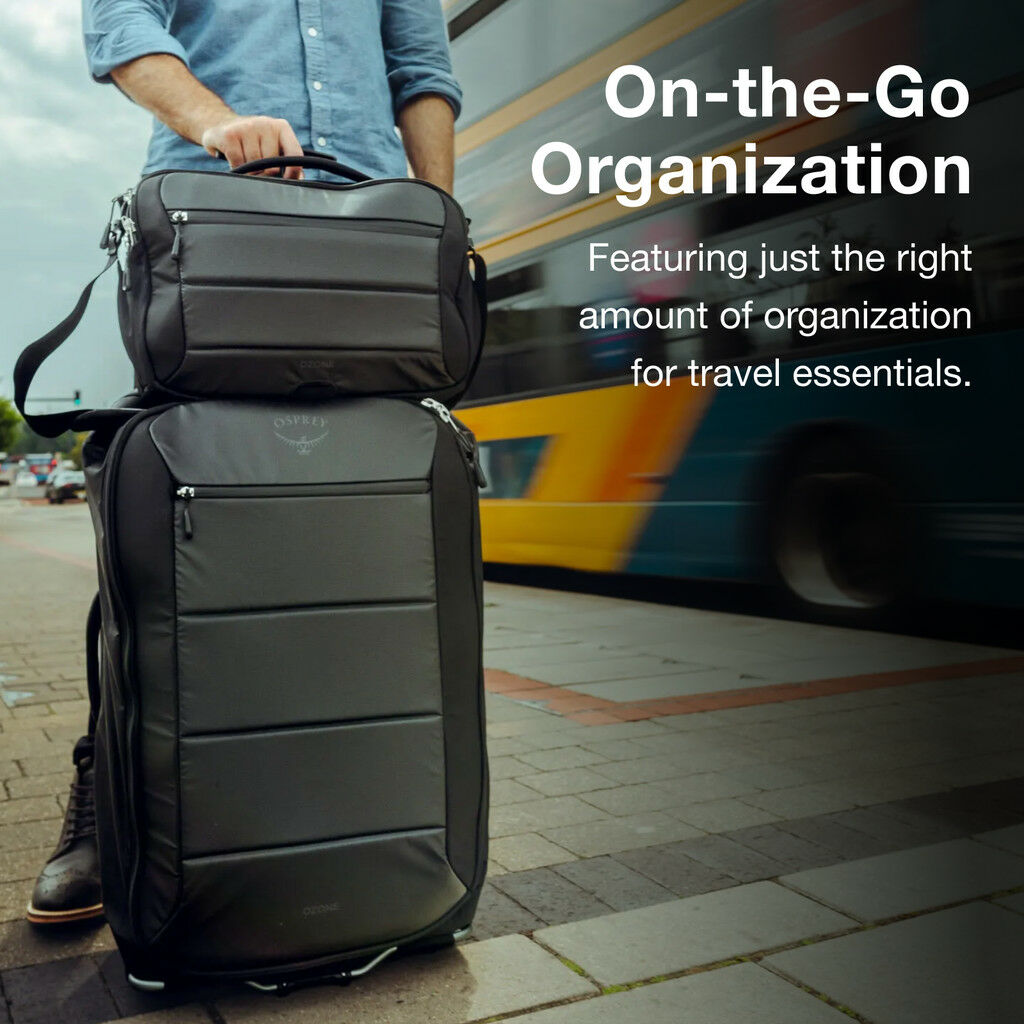 Person holding Osprey Ozone wheeled luggage with a bus passing by in the background.