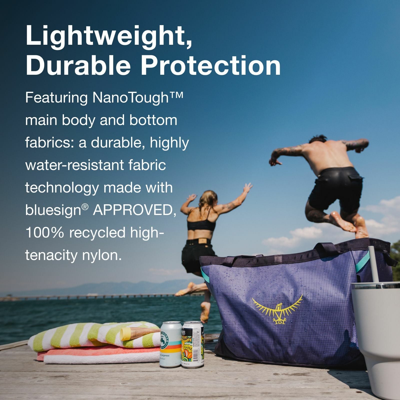 A vibrant beach scene featuring a durable, water-resistant bag with a logo, towels, and drinks, as two people jump into the water.